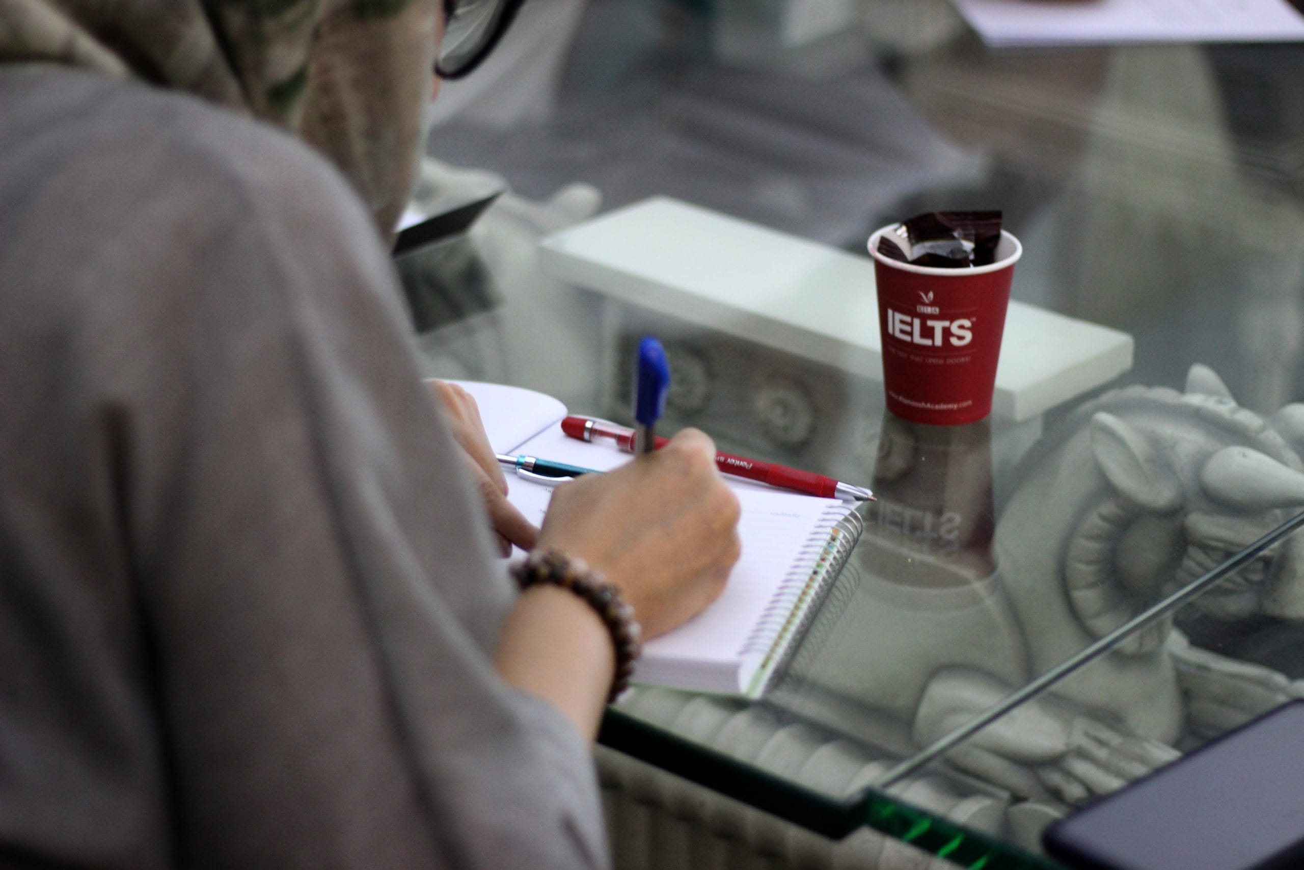 A cup showing the logo of IELTS on a table where a girl preparing for IELTS.